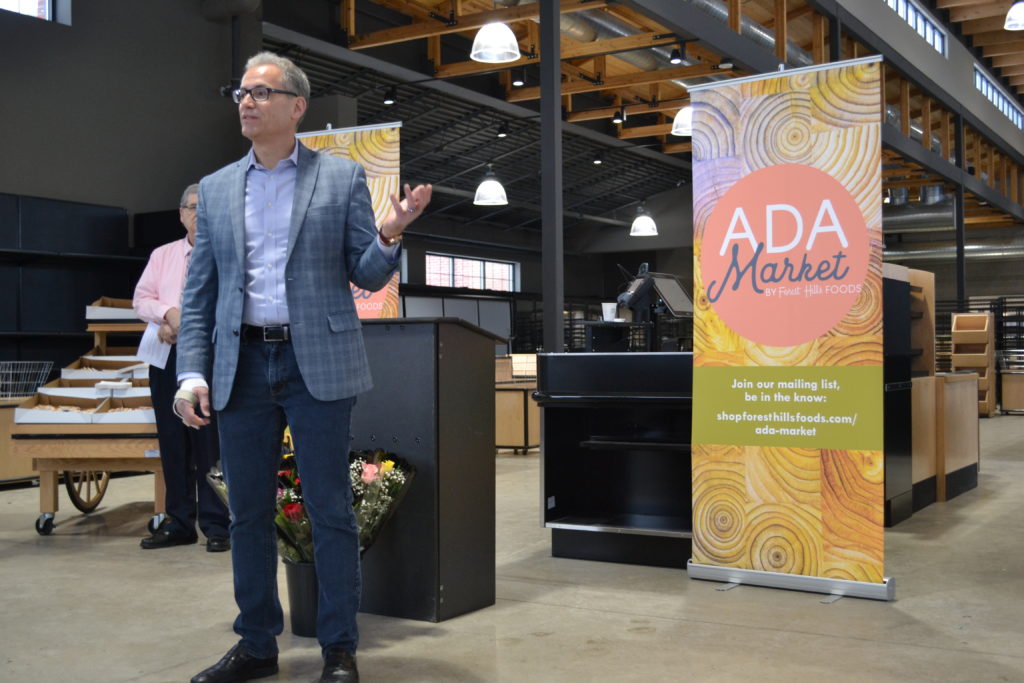man in professional clothing in front of a banner at the Ada Market