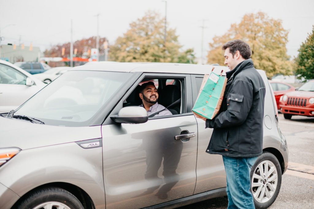 man with a paper bag standing near a man in a car