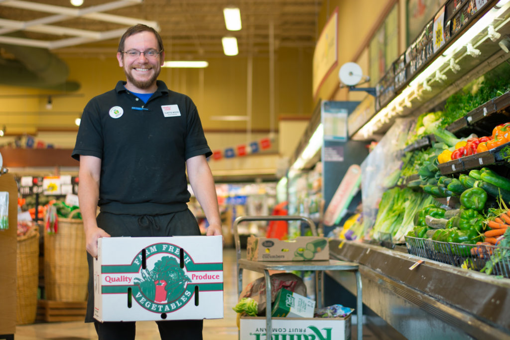 photo of a grocery store worker holding a box of produce in the produce section of the store