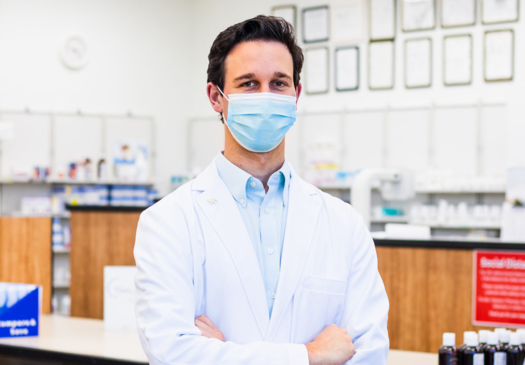 Caucasian man in medical mask and white lab coat in pharmacy setting