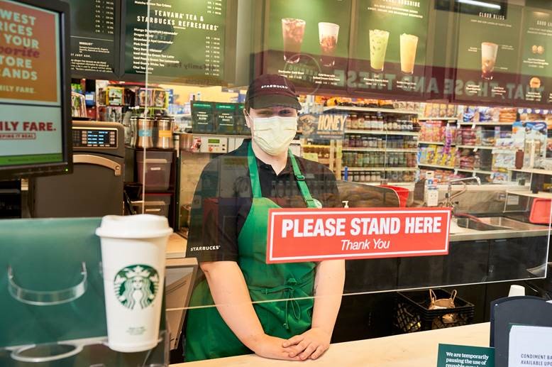 Starbucks worker in medical mask behind counter with hanging plexiglass between them and the photographer